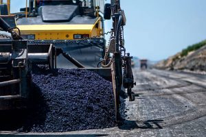 Industrial pavement machine laying fresh asphalt on highway construction site